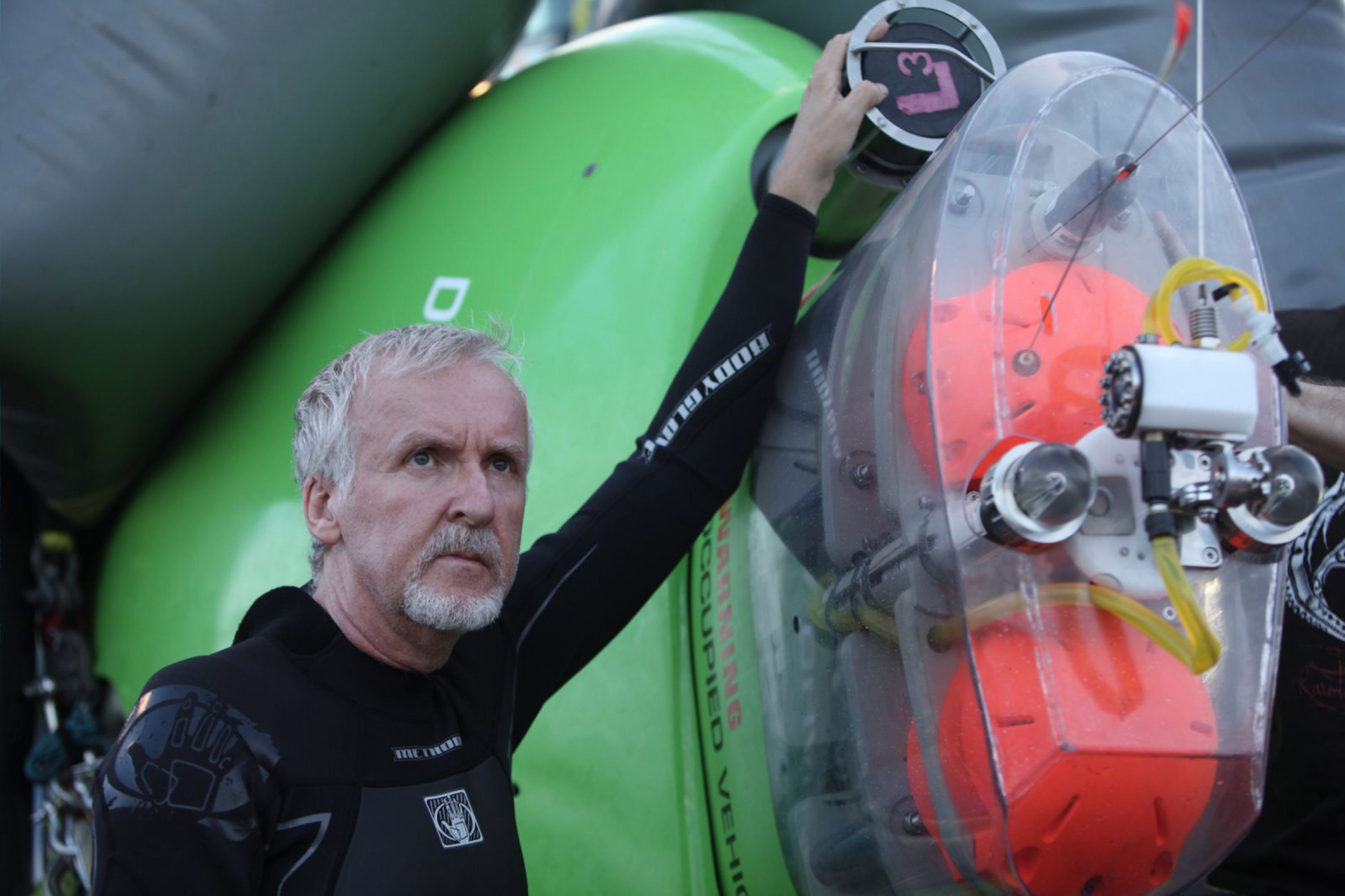 Photo of a man, James Cameron, wearing a wetsuit and standing beside technical instruments.  