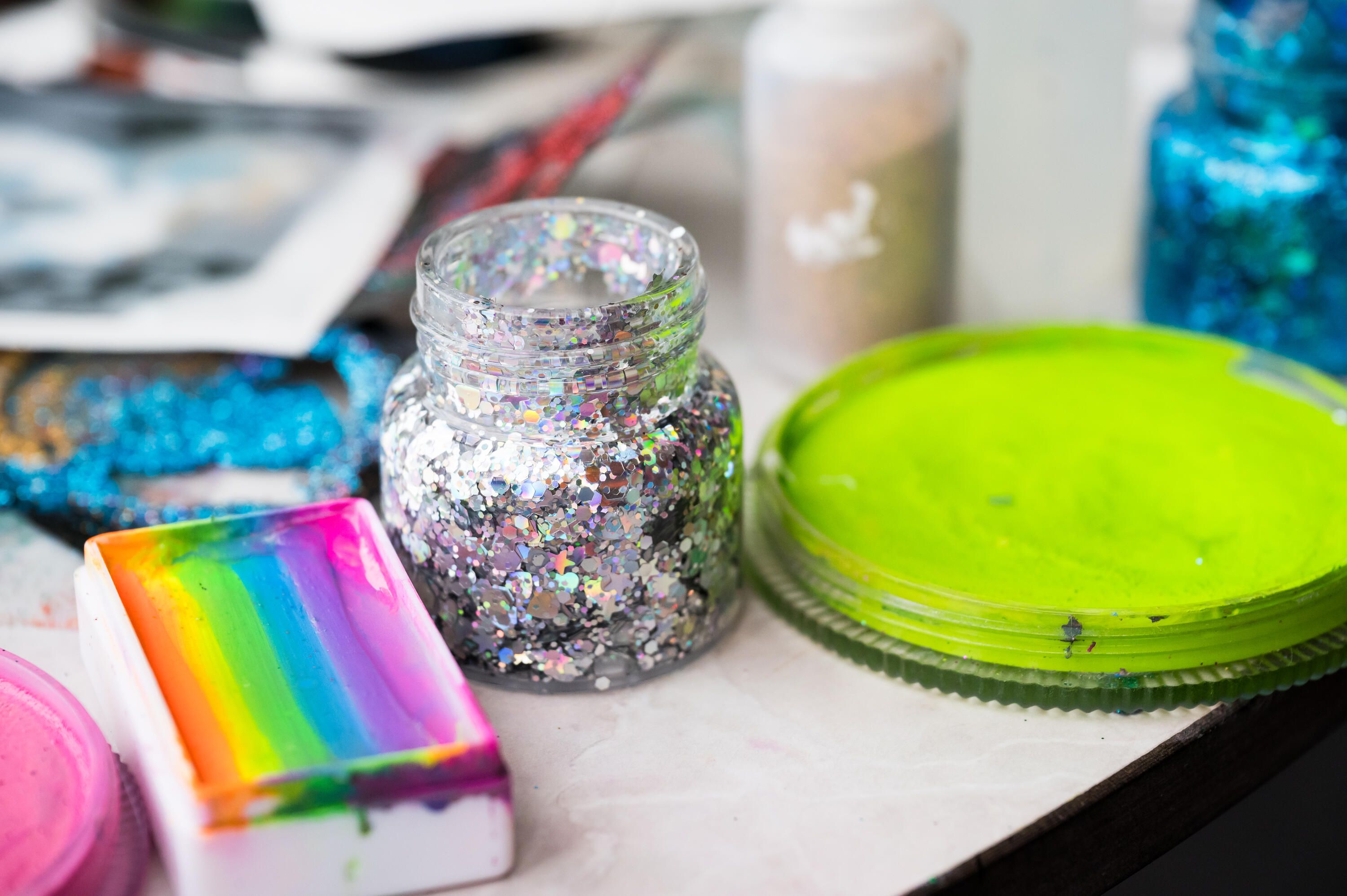 Close up photo of bright coloured and glitter face paints on a table.