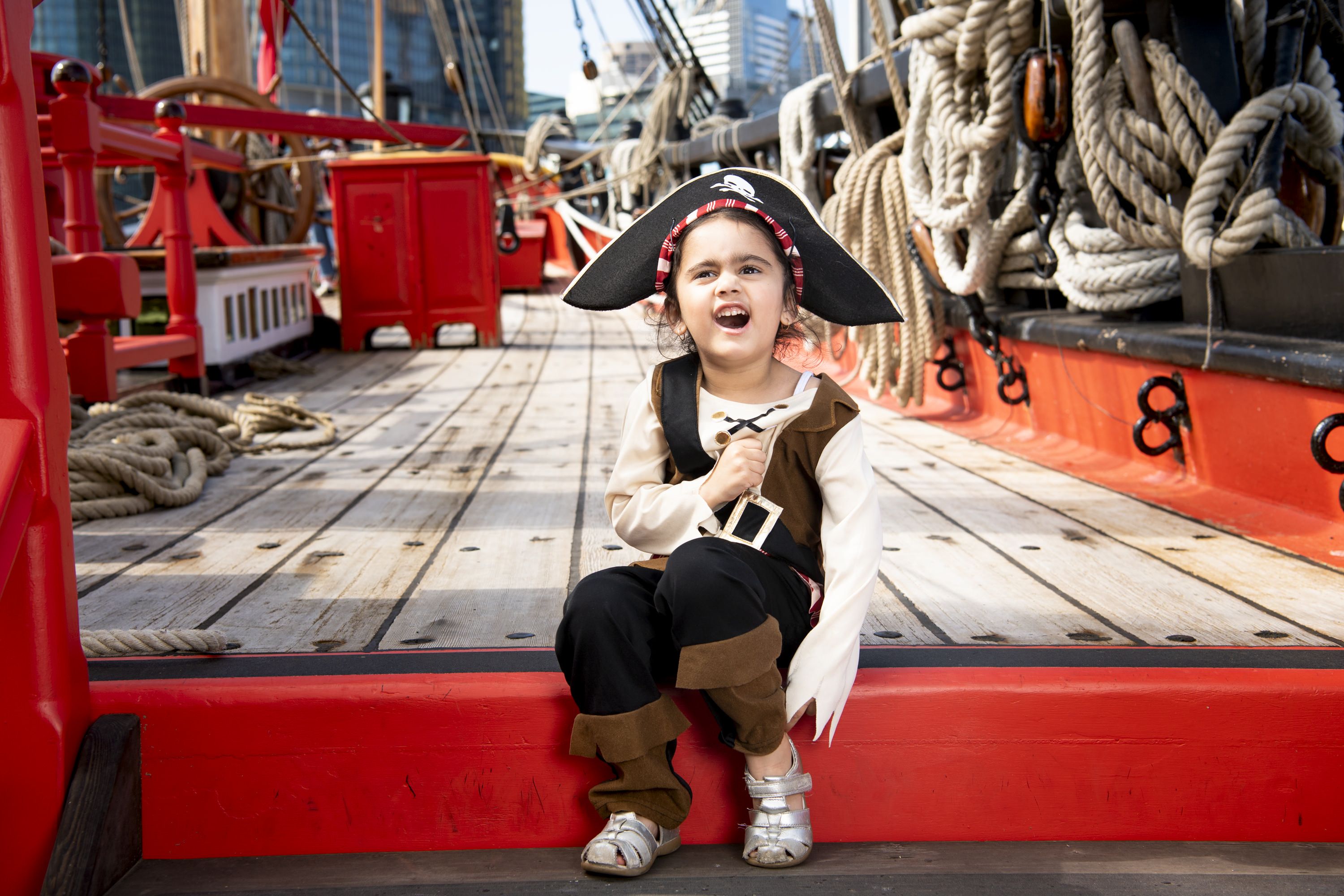 Photo showing a little girl dressed-up as a pirate on board a wooden tall ship.