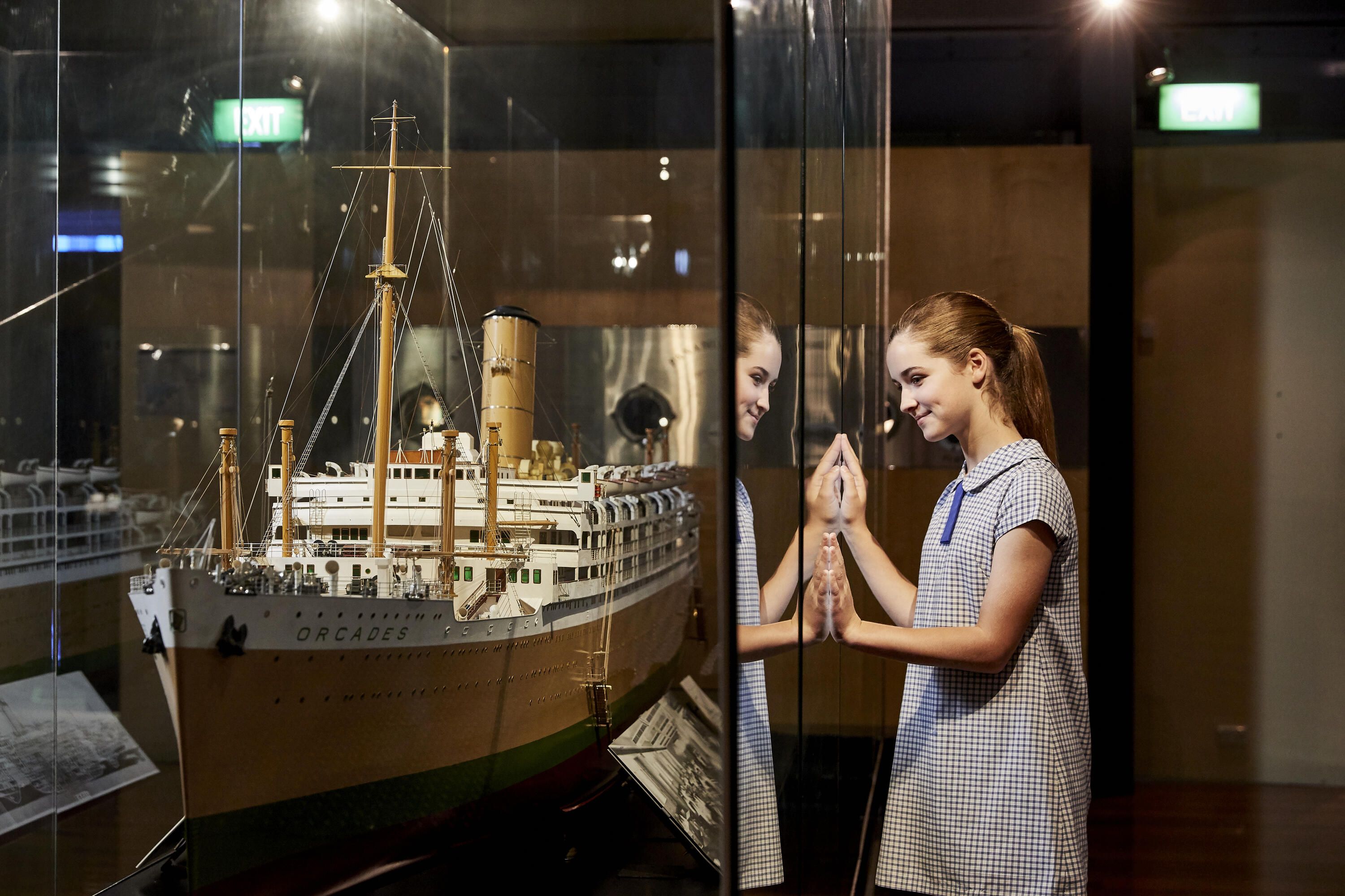 Photo of a girl in a schol uniform looking through a glass case at a large model ship.