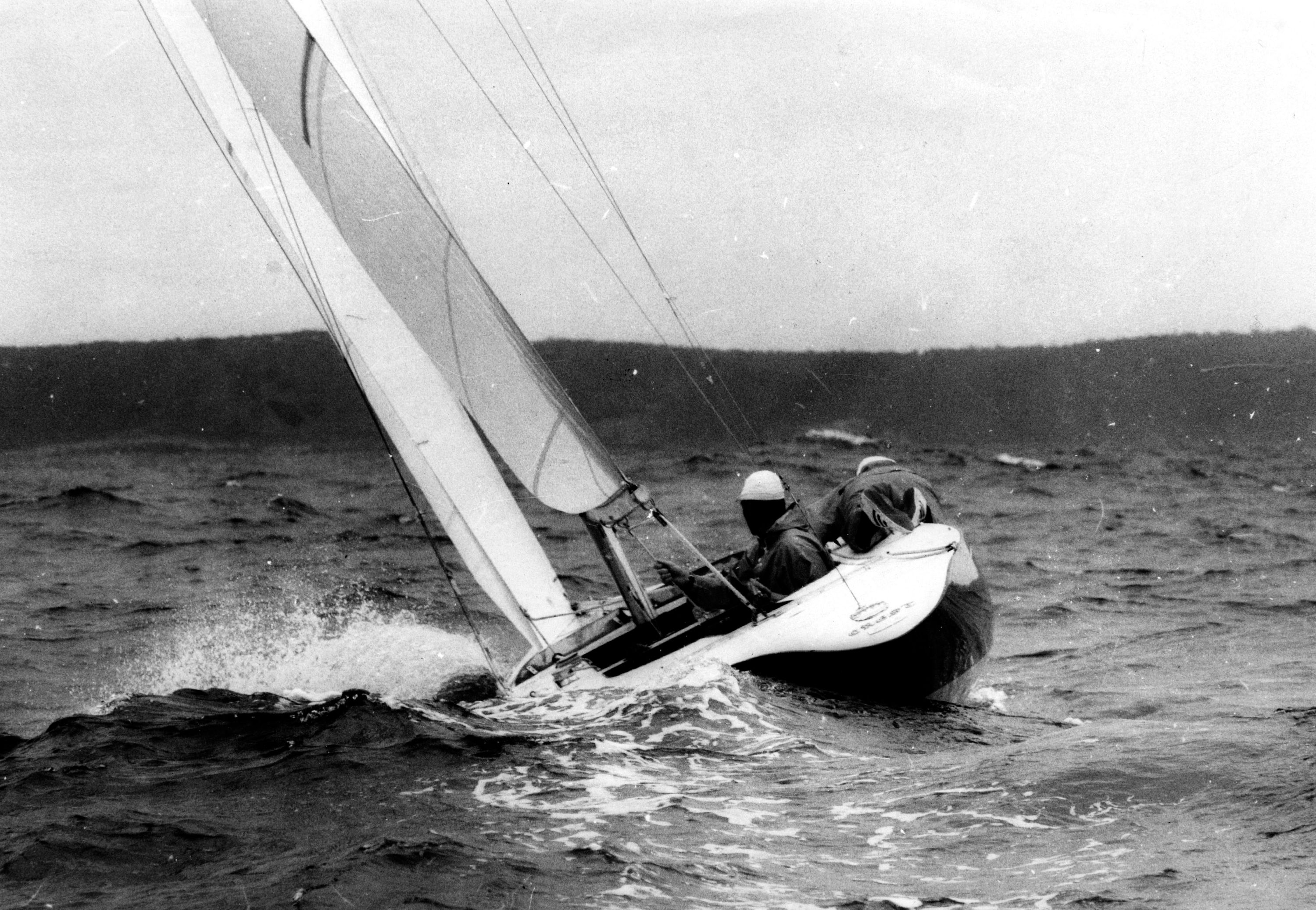 Black and white photo of a sailing boat with figures in it.