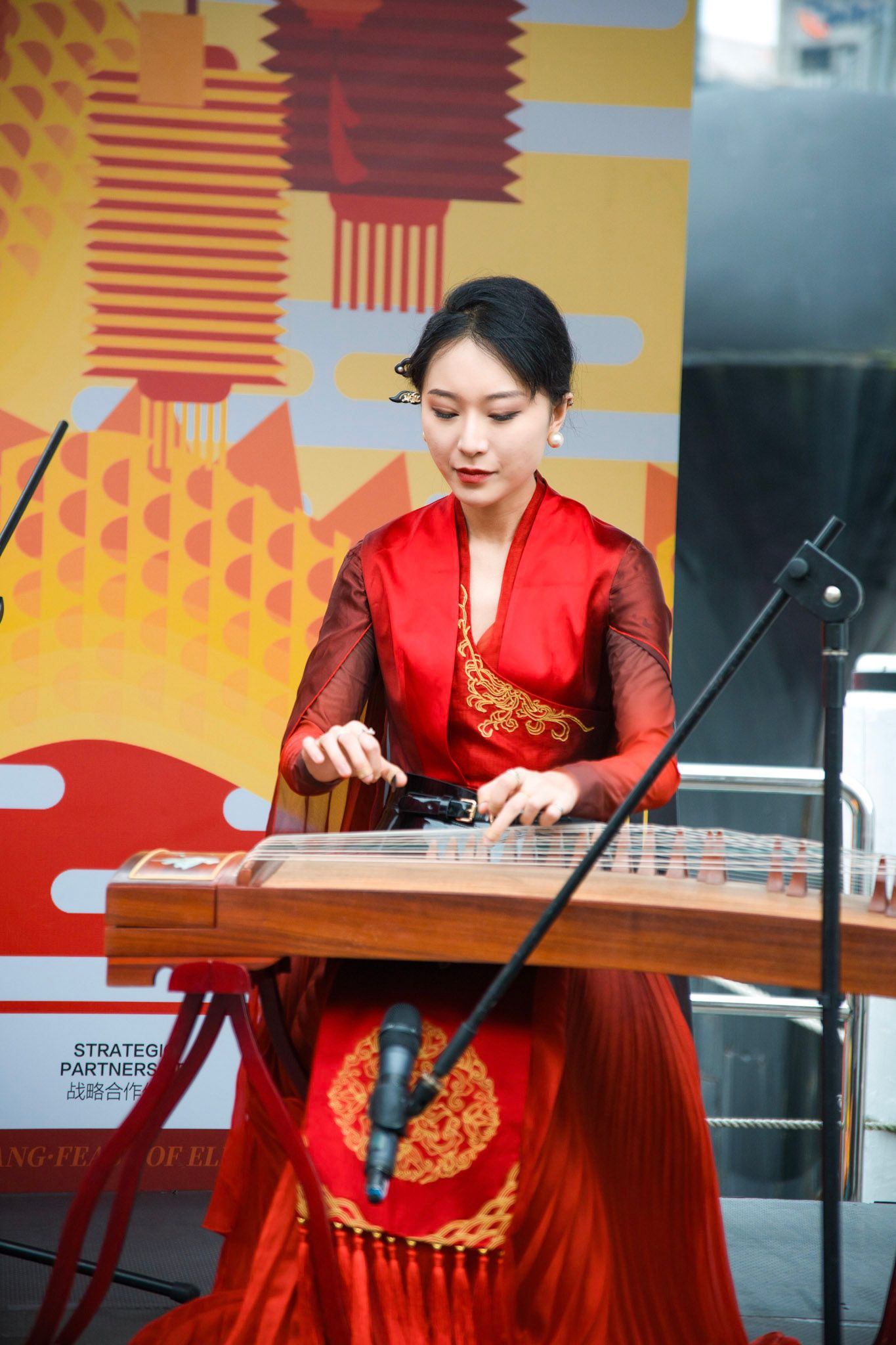 A woman, dressed in a red, Chinese dress, playing a string instrument/