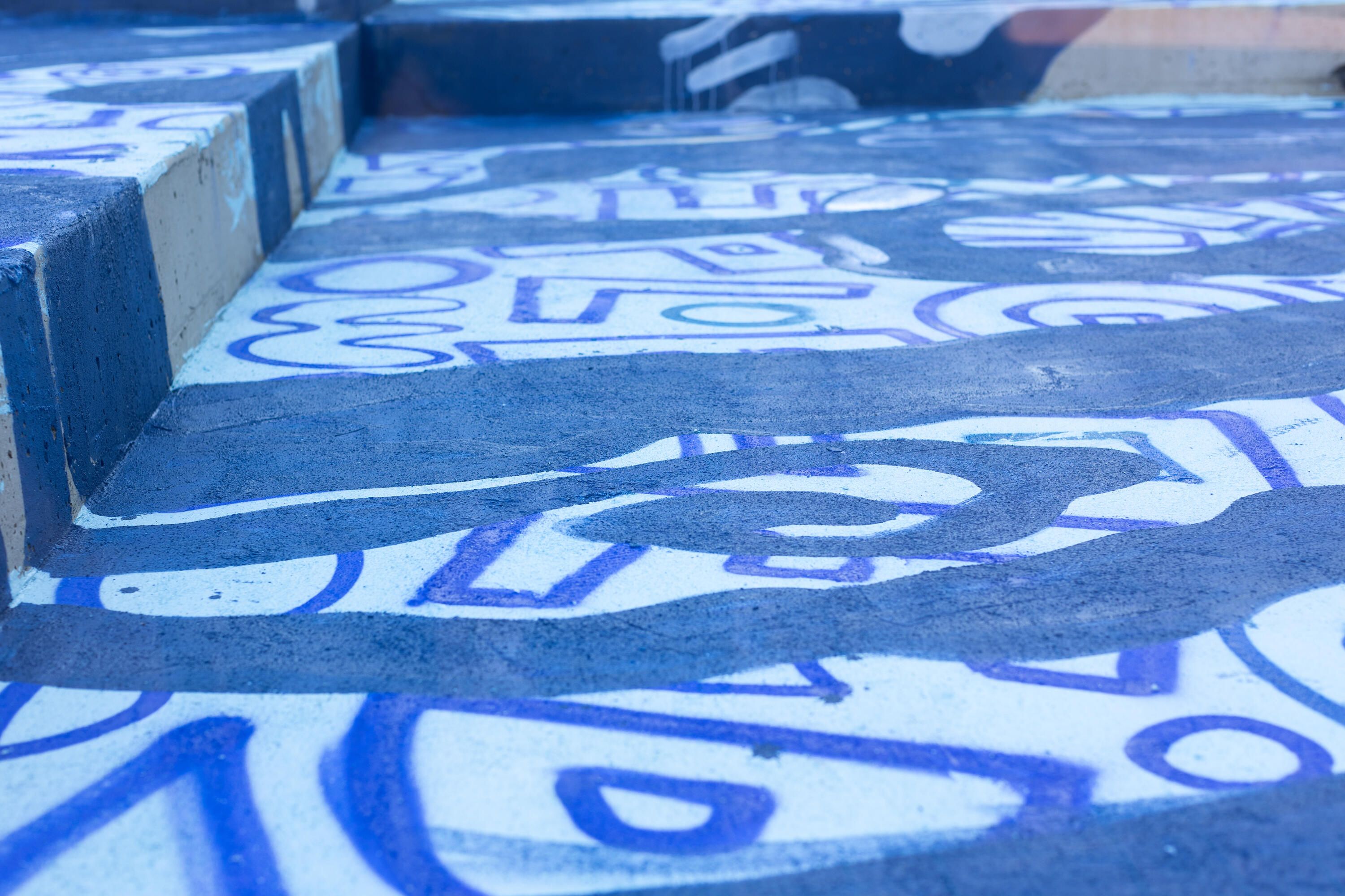 Close up photo showing a section of a mural painting in progress with light and dark blue paint.