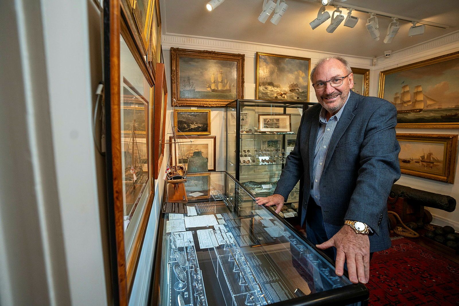 Photo of a man standing by a glass display case in a gallery space.
