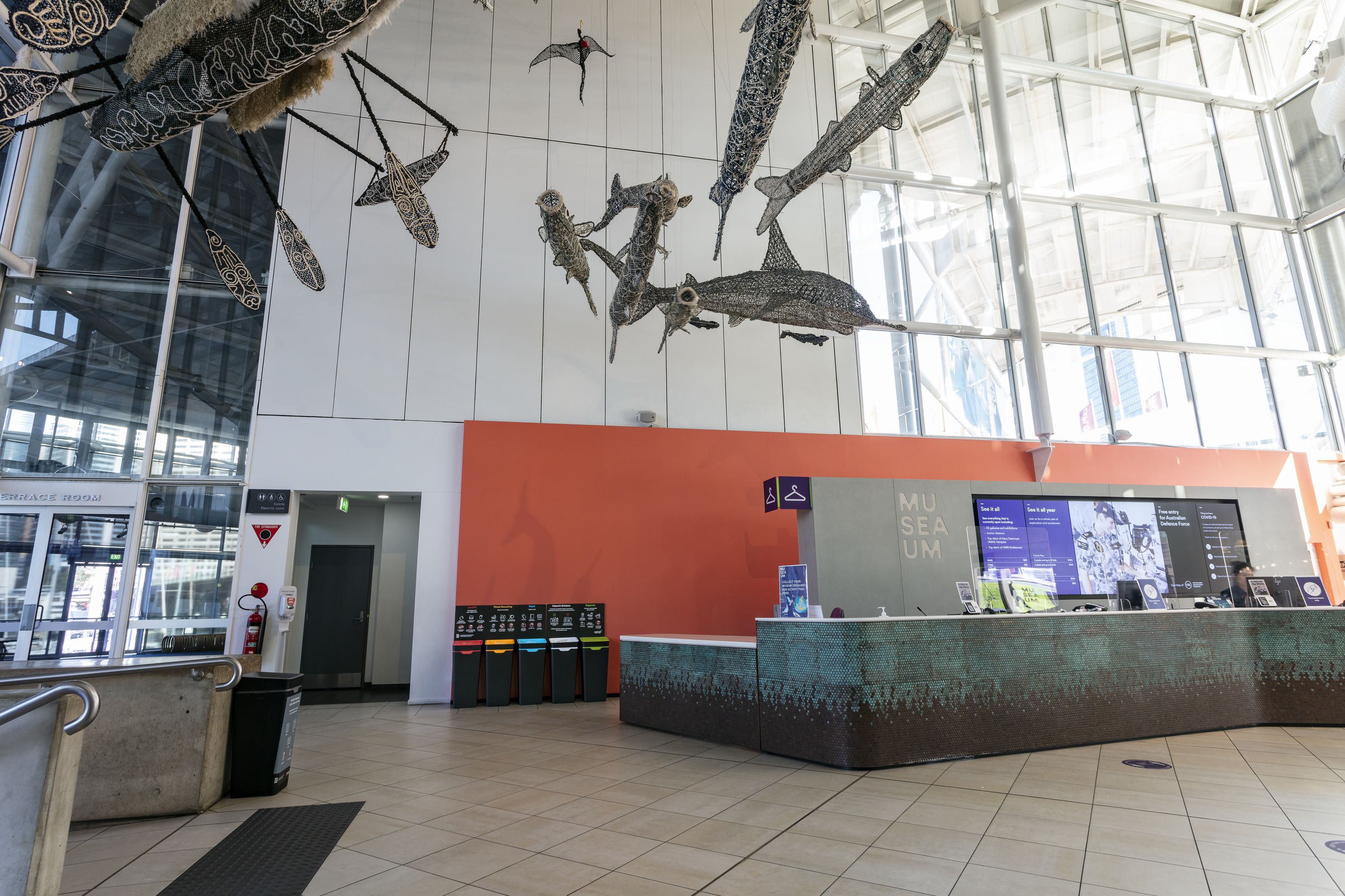 Photo showing the museum foyer near the front desk. The Ghost Net sculptures appear overhead. 